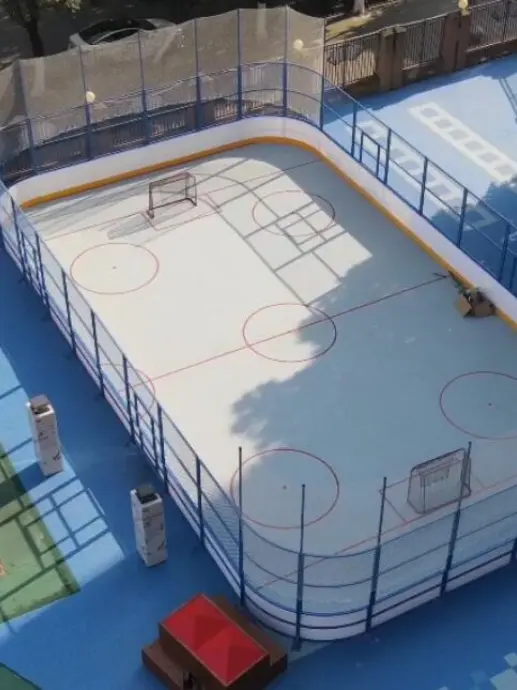 Outdoor synthetic ice hockey rink with protective barrier boards in a recreational area