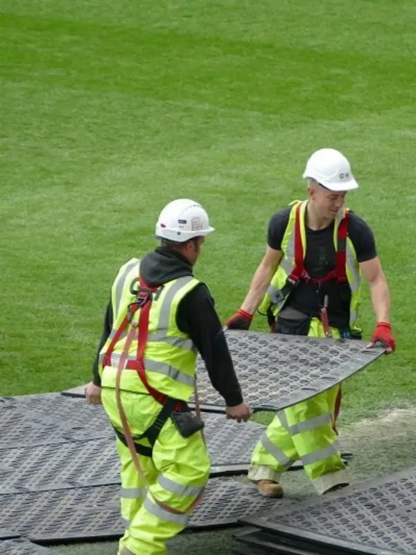 Workers manually installing lightweight interlocking plastic road mats on grass surface for temporary access road without heavy equipment